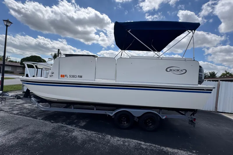 Slide: The Image of 2018 Beachcat 20 boat on trailer with blue canopy, parked outdoors under cloudy sky. - 2