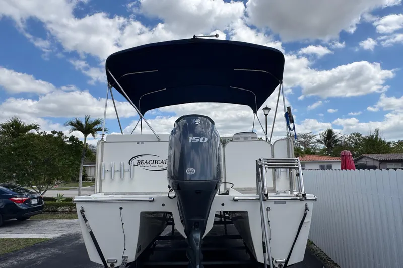 Slide: The Image of 2018 Beachcat 20 boat with 150 HP engine, parked outdoors under a blue sky. - 5