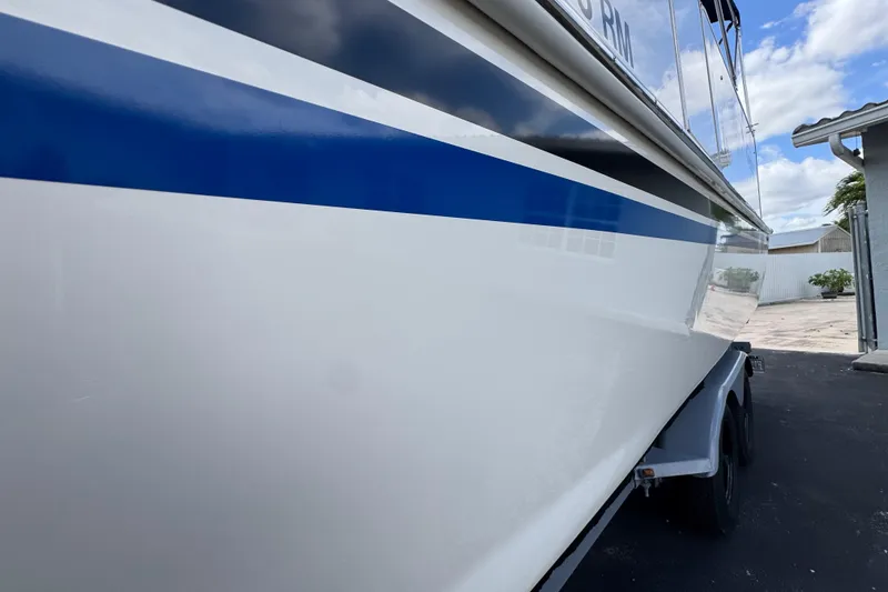 Slide: The Image of 2018 Beachcat 20 boat with blue stripe, parked on a trailer under a cloudy sky. - 9