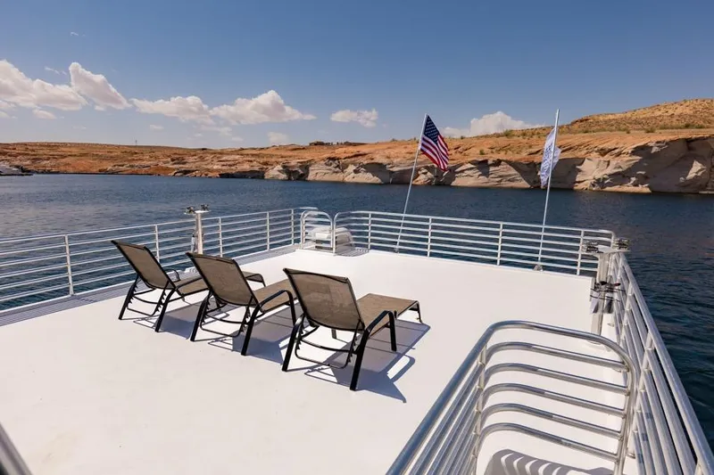 Slide: The Image of Rooftop deck of 2026 Sumerset Luxe III houseboat with lounge chairs and flags on a lake. - 13