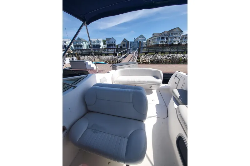 Slide: The Image of 1999 Chaparral Signature 240 boat interior with white seating, docked near waterfront homes. - 7