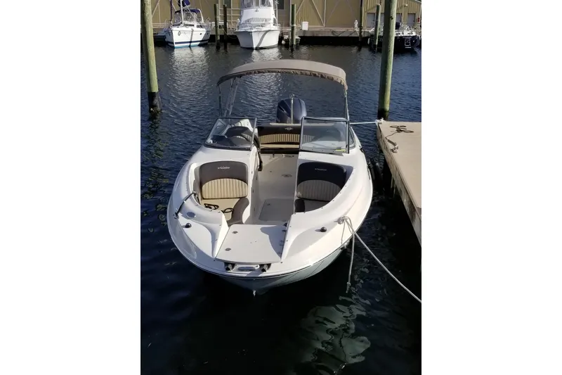 Slide: The Image of 2018 Stingray 234 LR boat docked at marina, featuring spacious seating and canopy. - 2