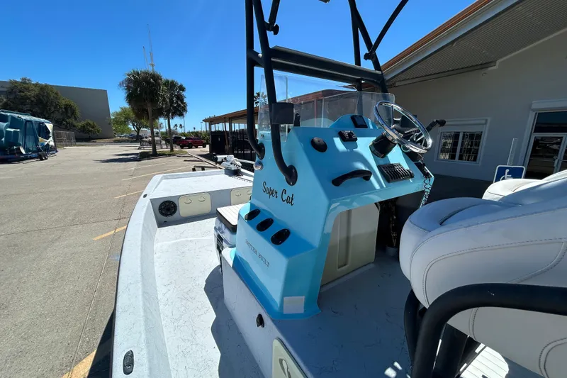 Slide: The Image of 2022 Stoner Super Cat boat with blue console and white seating, parked outdoors. - 7