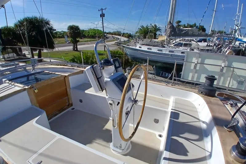 Slide: The Image of 1981 Gulfstar 44 sailboat cockpit with steering wheel, docked near palm trees and other boats. - 2