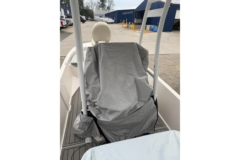 Slide: The Image of 2024 Carolina Skiff 192 JLS boat seat covered, parked outdoors near blue buildings. - 16