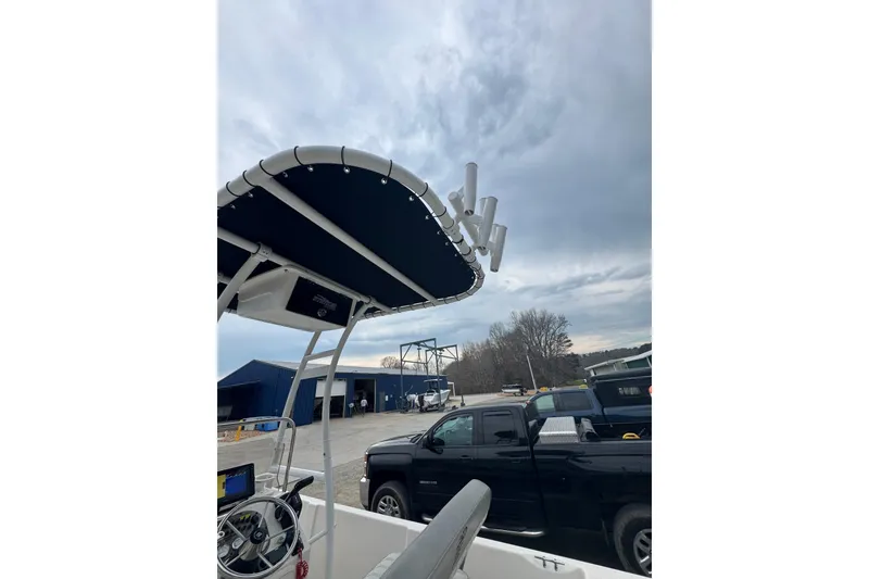 Slide: The Image of 2024 Carolina Skiff 192 JLS boat with T-top and rod holders, parked near trucks. - 6