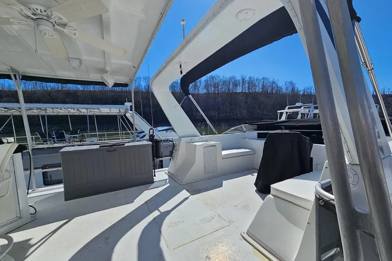 Slide: The Image of 2001 Sumerset 16x79 houseboat deck with seating, canopy, and storage, docked by a wooded shoreline. - 60