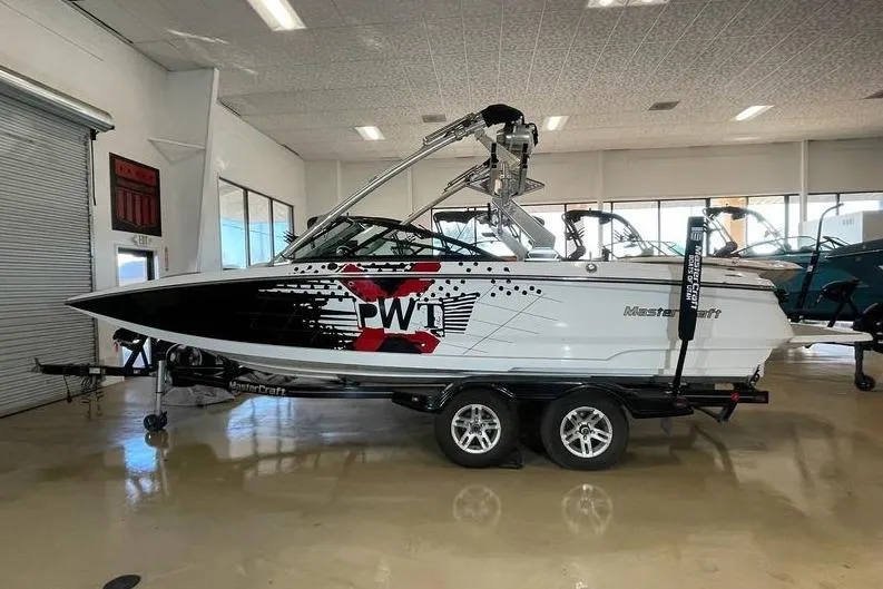 The Image of 2010 MasterCraft XStar boat on trailer in showroom, featuring bold graphics. - 1