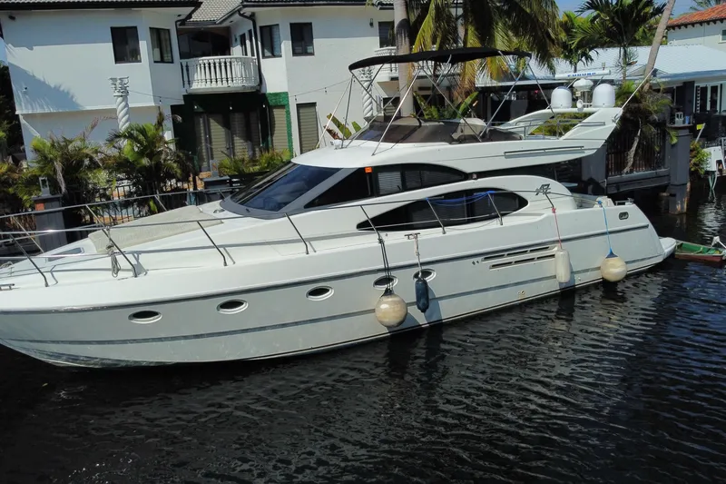 The Image of 1998 Azimut 52 yacht docked near waterfront homes, surrounded by lush greenery. - 0