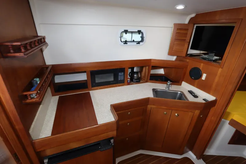 Slide: The Image of 2002 Mainship Pilot 34 galley with wood cabinetry, sink, microwave, and TV. - 49