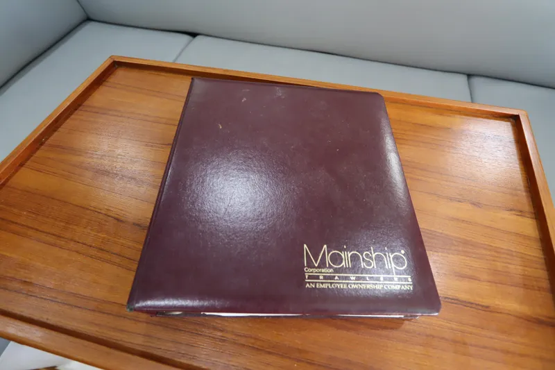 Slide: The Image of Mainship Pilot 34 2002 manual on wooden table, showcasing boat documentation. - 68