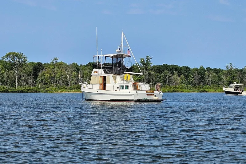 Slide: The Image of 1989 Grand Banks 36 Classic yacht on a serene lake with lush green shoreline. - 56