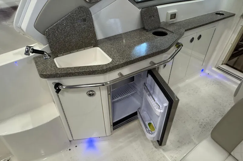 Slide: The Image of 2015 Chaparral 330 Signature boat kitchenette with sink, countertop, and open mini fridge. - 12