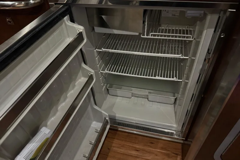 Slide: The Image of Open refrigerator inside 2015 Chaparral 330 Signature boat, showcasing empty shelves and door compartments. - 27