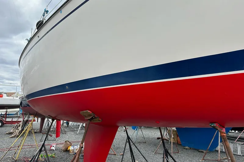 The Image of 1984 Pearson 34 sailboat on stands, featuring a red hull and blue stripe. - 1