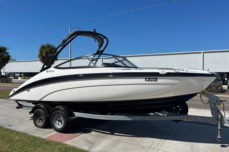 The Image of 2017 Yamaha AR210 boat on trailer, parked outdoors under clear blue sky. - 1