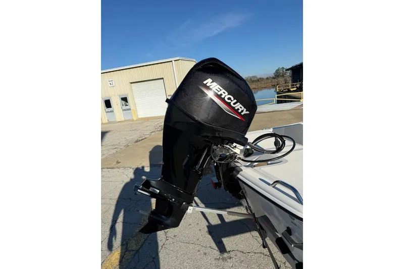 Slide: The Image of Outboard motor on a 2025 Mako Pro Skiff 15 CC boat, parked near a warehouse. - 11