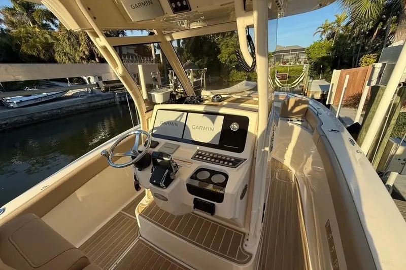 Slide: The Image of 2024 Scout 277 LXF boat interior with Garmin navigation system, docked near lush greenery. - 8