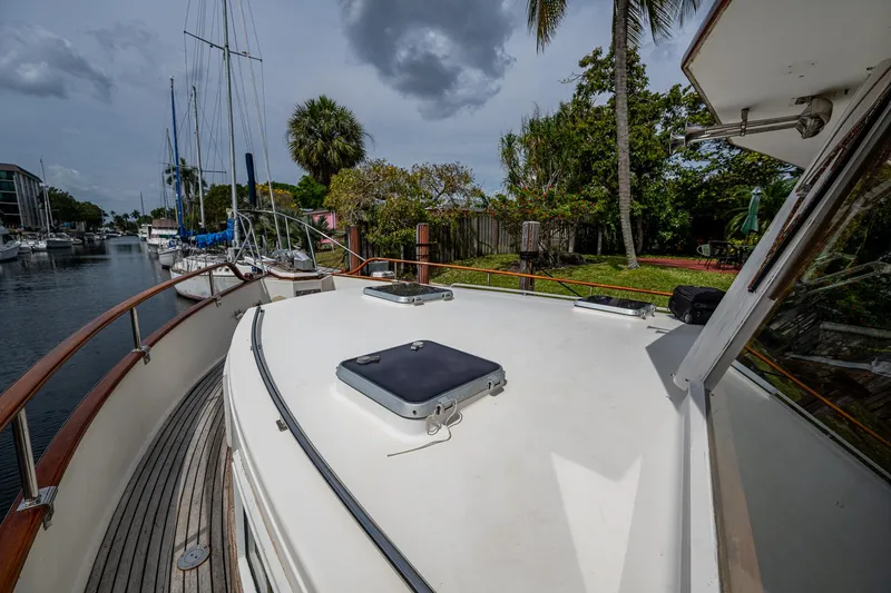Slide: The Image of 1990 Grand Banks 46 Classic yacht deck with wooden railings, docked near lush greenery. - 7