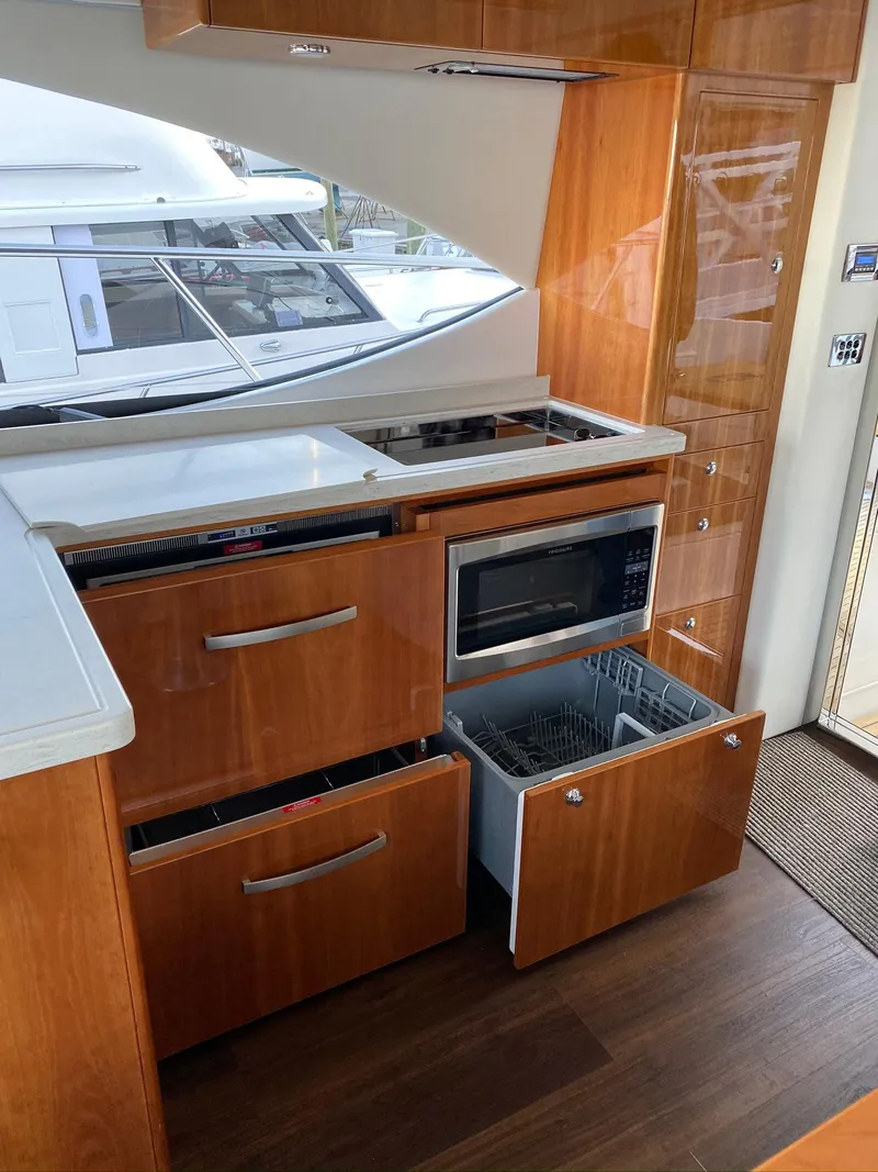 Slide: The Image of 2016 Riviera 5000 Sport Yacht kitchen with wood cabinetry, microwave, and dishwasher. - 31