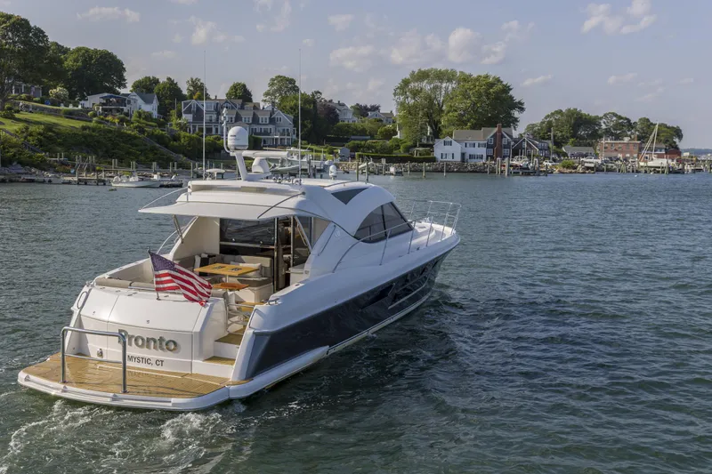 Slide: The Image of 2016 Riviera 5000 Sport Yacht cruising near coastal homes, displaying an American flag. - 4