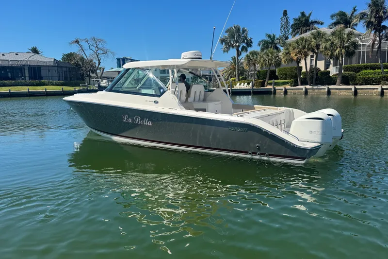 Slide: The Image of 2016 Pursuit DC 325 Dual Console boat on calm water near a lush shoreline. - 15