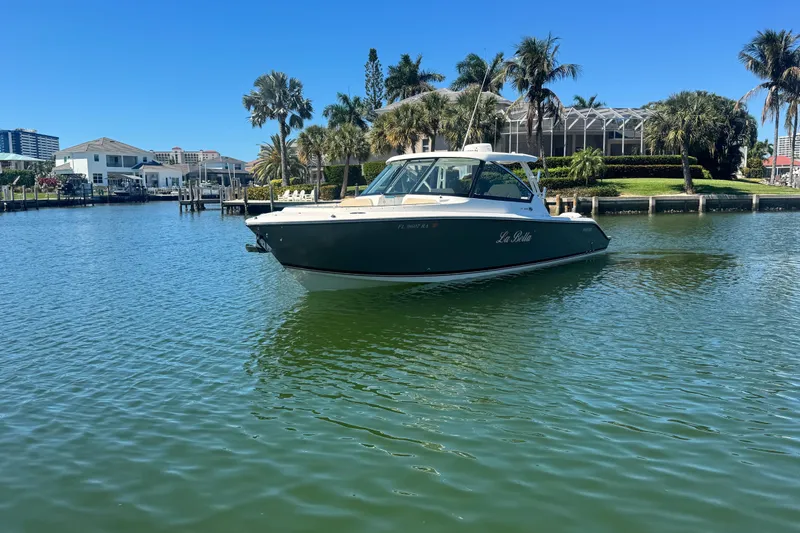 Slide: The Image of 2016 Pursuit DC 325 Dual Console boat on calm water, surrounded by palm trees and waterfront homes. - 2