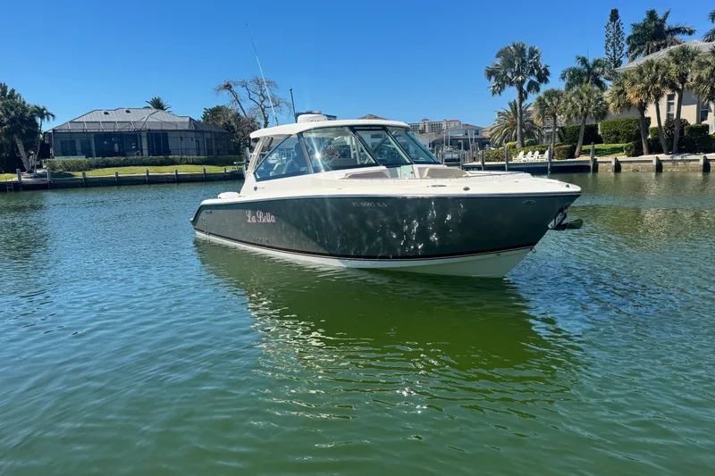 Slide: The Image of 2016 Pursuit DC 325 Dual Console boat on calm water, surrounded by waterfront homes. - 42