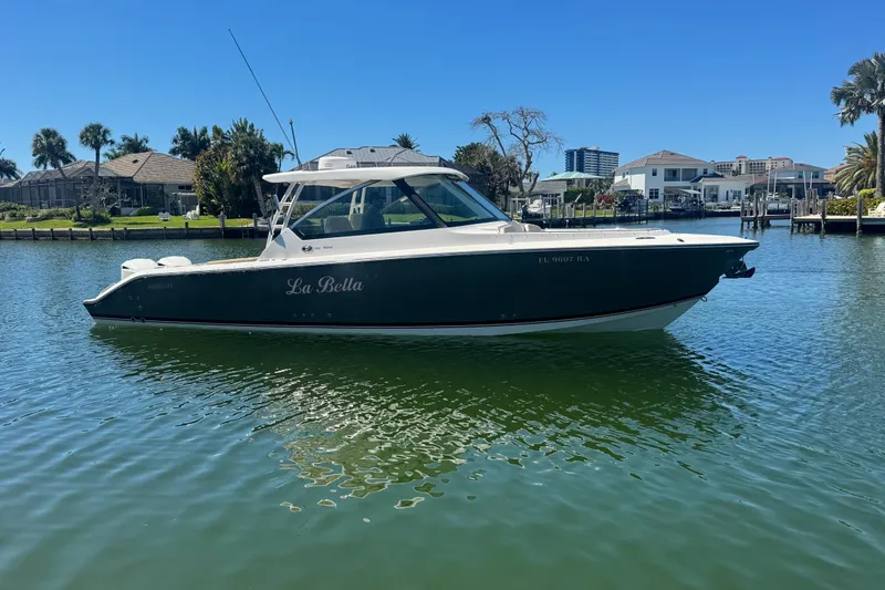 Slide: The Image of 2016 Pursuit DC 325 Dual Console boat on calm water, with waterfront homes in the background. - 43