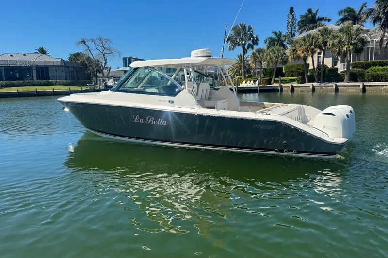 Slide: The Image of 2016 Pursuit DC 325 Dual Console boat on calm water, surrounded by palm trees. - 44