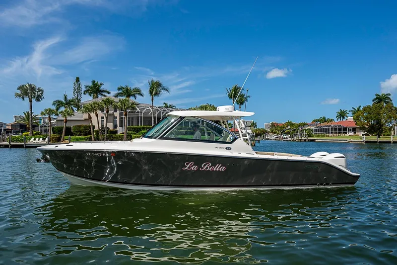 Slide: The Image of 2016 Pursuit DC 325 Dual Console boat on water, with palm trees and houses in background. - 47