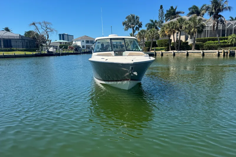 Slide: The Image of 2016 Pursuit DC 325 Dual Console boat on calm water, surrounded by palm trees and houses. - 5