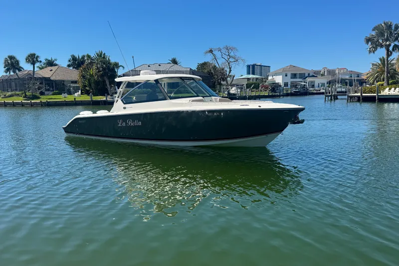Slide: The Image of 2016 Pursuit DC 325 Dual Console boat on calm water near waterfront homes. - 8