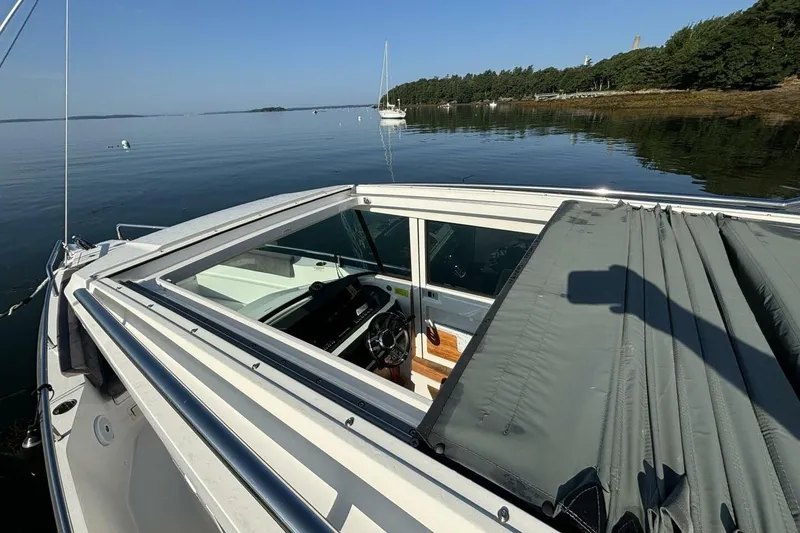Slide: The Image of 2019 Axopar 28 Cabin boat on calm water, featuring open roof and scenic shoreline. - 21