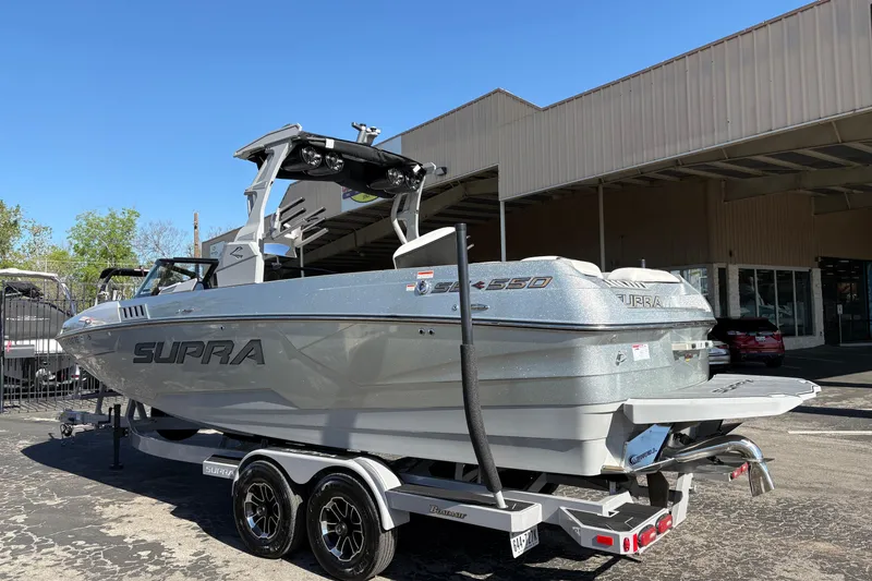 Slide: The Image of 2021 Supra SE 550 boat on trailer, parked outside a building under clear blue sky. - 6