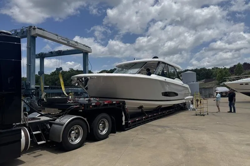 Slide: The Image of 2025 Regal LX43 yacht on trailer under cloudy sky at marina. - 91