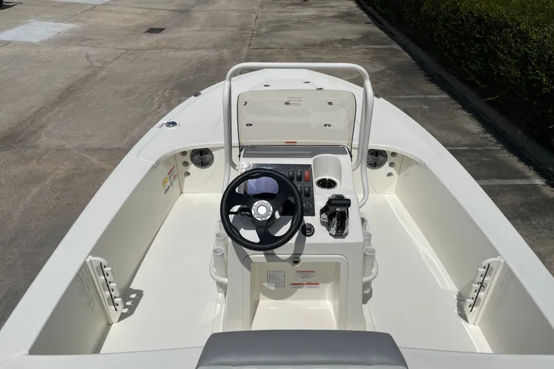 Slide: The Image of 2026 Mako 18 Pro Skiff boat interior with steering wheel and console, parked on concrete. - 11