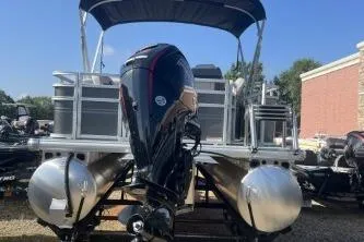 Slide: The Image of 2026 Sun Tracker Fishin' Barge 20 DLX pontoon boat with outboard motor, parked outdoors. - 1