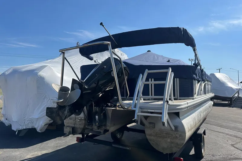 Slide: The Image of 2023 Bennington 21 SL pontoon boat with cover, parked on a trailer under clear blue sky. - 3
