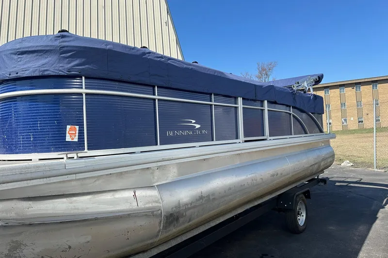 Slide: The Image of 2023 Bennington 21 SL pontoon boat with blue cover, parked outdoors. - 4