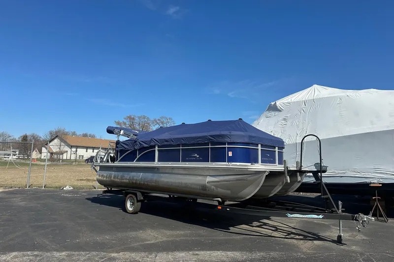 Slide: The Image of 2023 Bennington 21 SL pontoon boat covered, parked on a trailer under clear blue sky. - 5