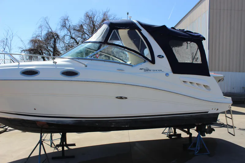Slide: The Image of 2006 Sea Ray Sundancer 260 boat on stands, white hull, black canopy, outdoor setting. - 2