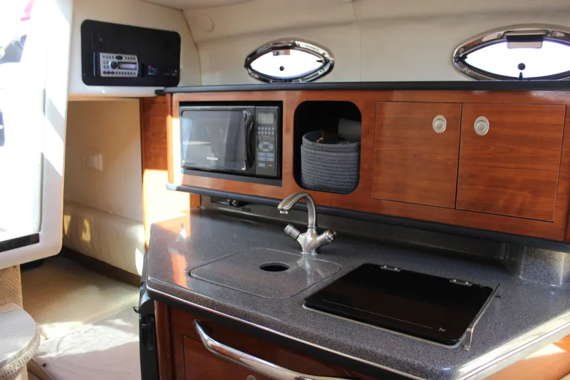 Slide: The Image of 2006 Sea Ray Sundancer 260 interior with kitchenette, featuring microwave, sink, and wooden cabinets. - 28