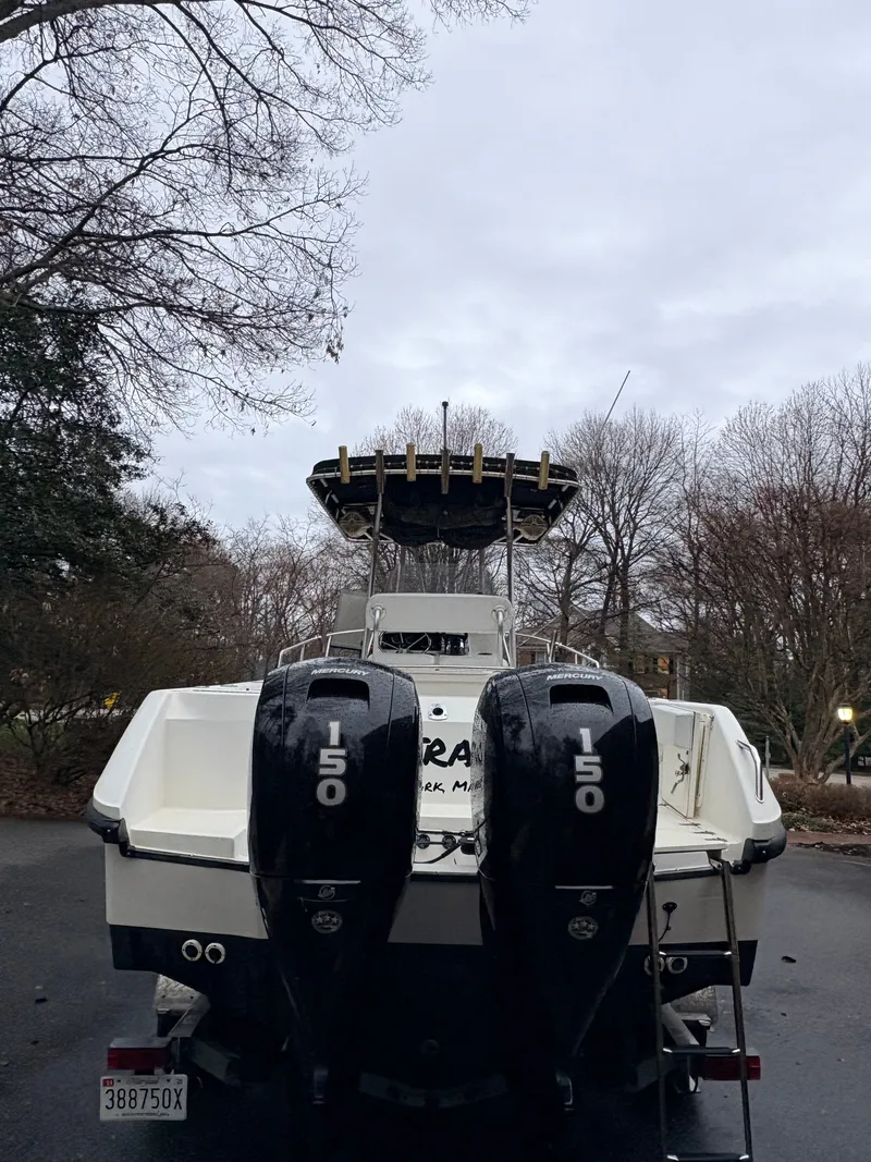 Slide: The Image of 1999 Boston Whaler 230 Outrage with twin outboard engines, parked outdoors. - 5