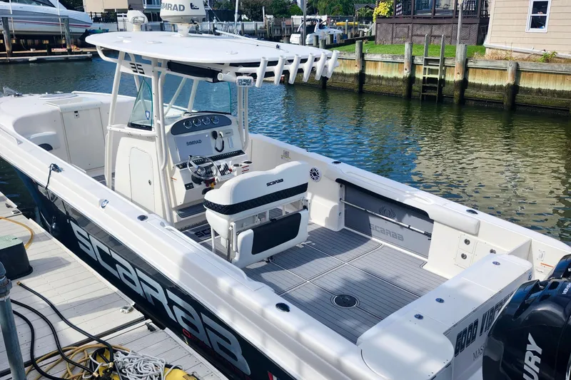 Slide: The Image of 2014 Wellcraft 35 Scarab Sport boat docked by the water, featuring a sleek design. - 2