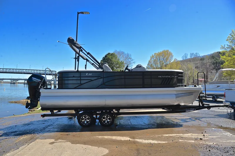 Slide: The Image of 2022 Bennington 22 L pontoon boat on trailer by riverside under clear blue sky. - 15