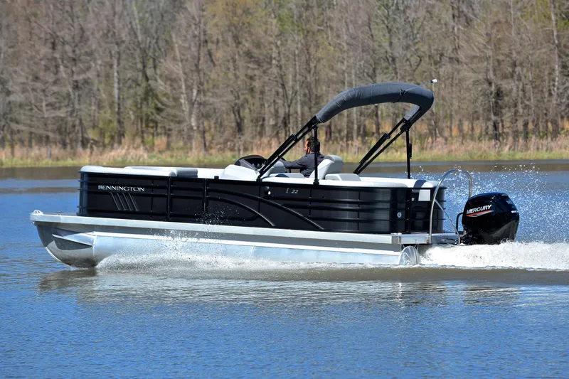 Slide: The Image of 2022 Bennington 22 L pontoon boat cruising on a lake with trees in the background. - 4