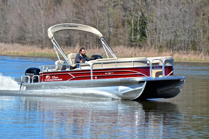 The Image of 2019 Sun Tracker SportFish 22 DLX pontoon boat cruising on a calm lake. - 1