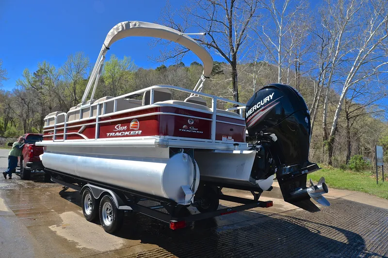 Slide: The Image of 2019 Sun Tracker SportFish 22 DLX pontoon boat on trailer, parked near a wooded area. - 12
