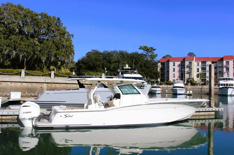Slide: The Image of 2021 Scout 355 LXF boat docked in a marina with buildings and trees in the background. - 2